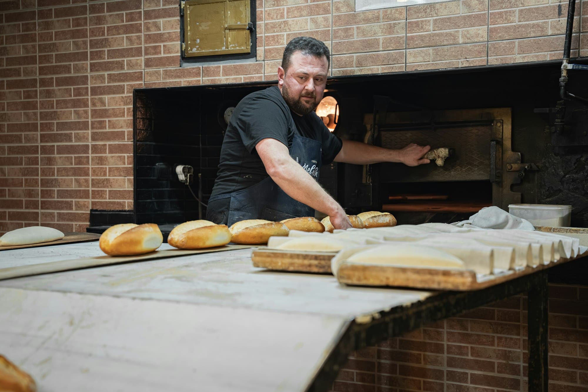 Baker loading loaves into a brick oven