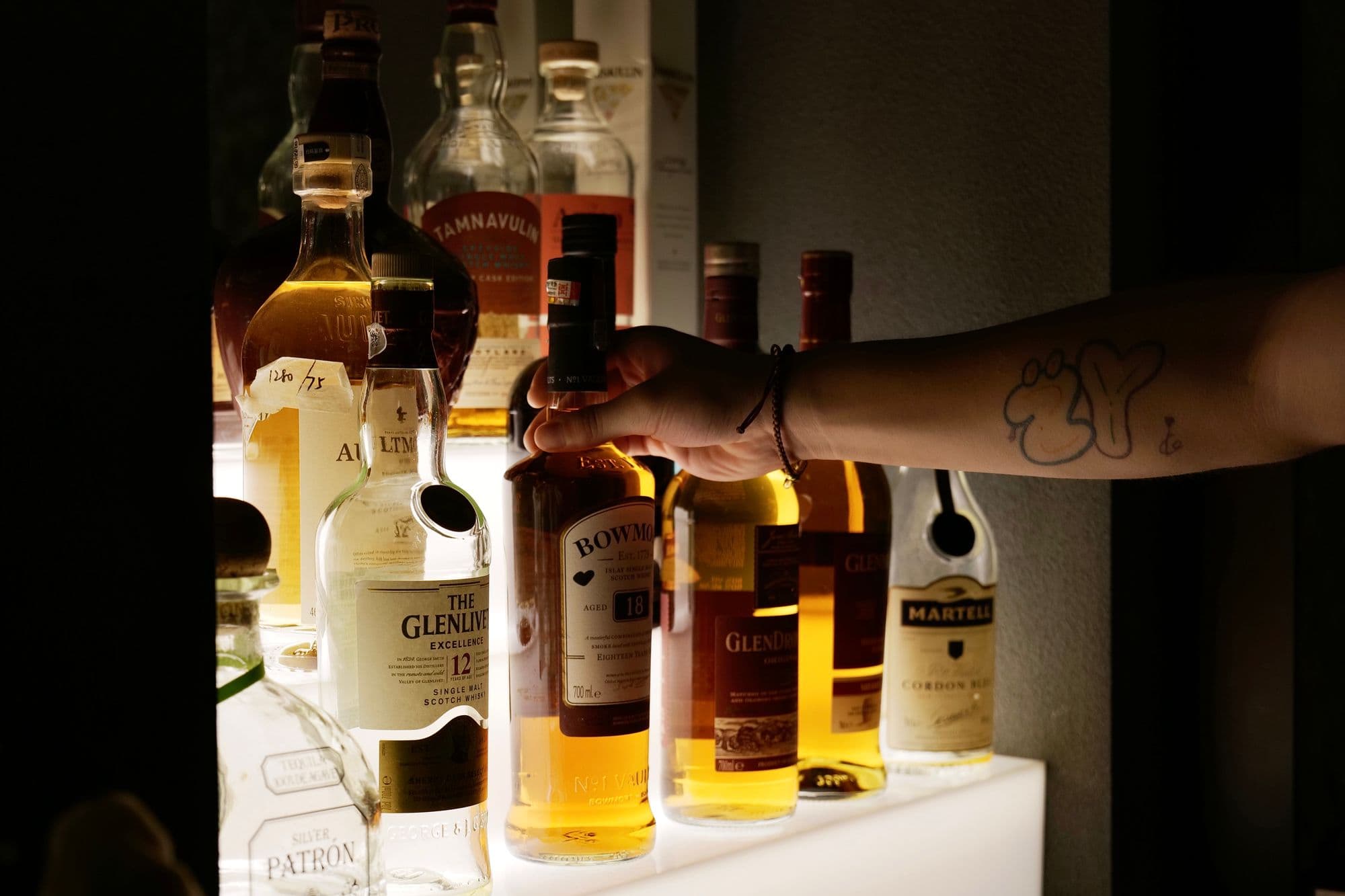 Hand taking a whisky bottle from a lit bar shelf